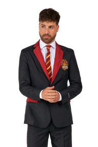 A man dressed in the Suitmeister Harry Potter Suit Gryffindor™ is wearing a black suit with red accents and a red and yellow striped tie. The jacket features a crest on the left side. He stands with his hands together, slightly facing right.