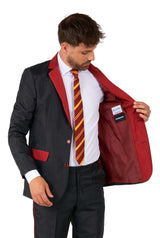 A man wearing the Harry Potter Suit Gryffindor™ by Suitmeister, featuring red accents and a red and yellow striped tie, opens the jacket to reveal its red lining with the label visible on the inside.