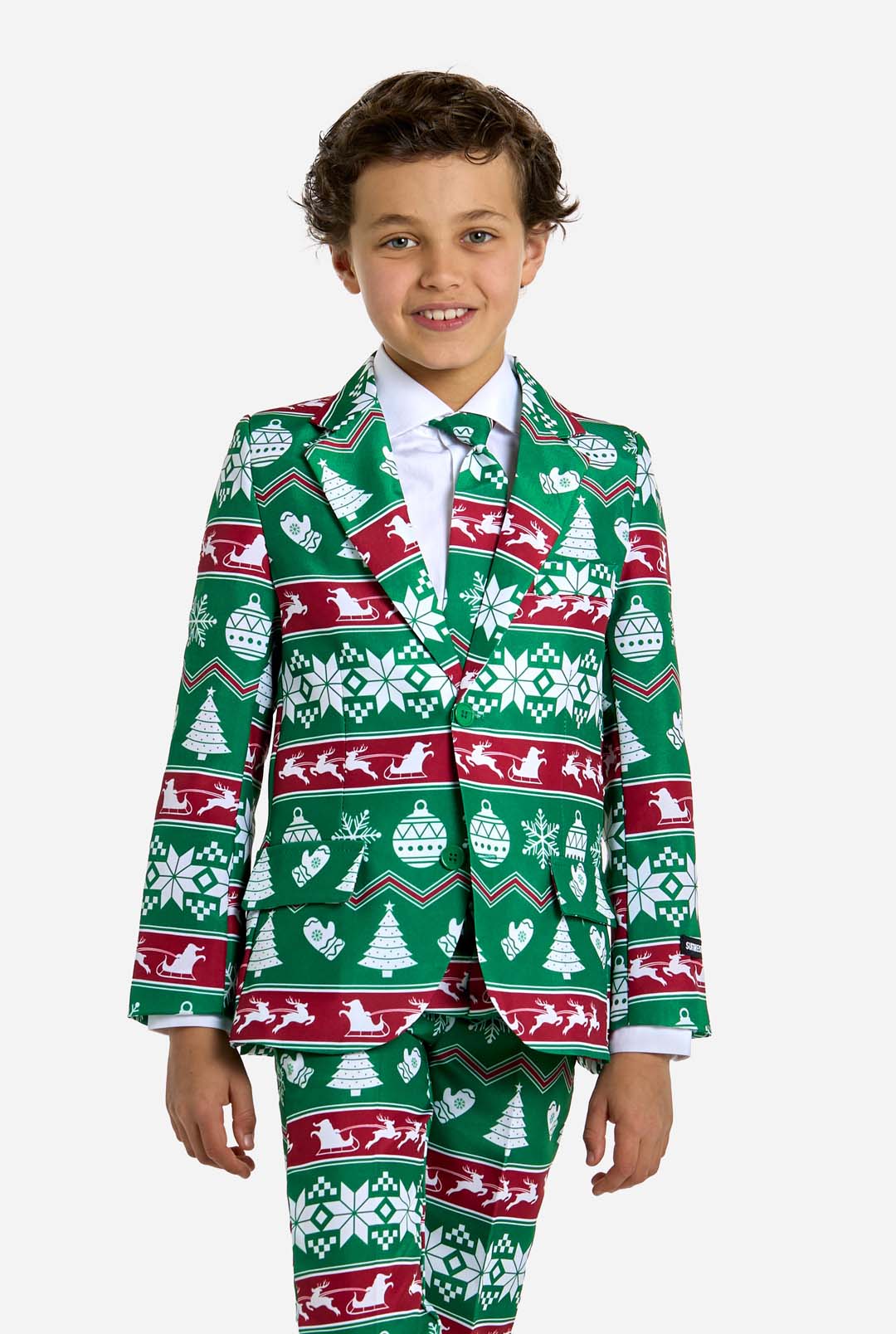 A young boy smiles while wearing the Christmas Suit Green Nordic by Suitmeister, featuring a festive pattern with snowflakes, trees, and reindeer in green and red. He is standing against a plain white background.