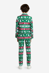 A child, with short dark hair, is standing facing away, dressed in the "Christmas Suit Green Nordic" by Suitmeister. The suit features festive red and white holiday patterns of snowflakes, Christmas trees, and reindeer. The child completes the look with white shoes against a plain white background.