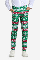 A person is dressed in the Suitmeister "Christmas Suit Green Nordic," showcasing bright green holiday-themed pants adorned with red and white festive patterns, including snowflakes, Santa, reindeer, and Christmas trees. They pair this with a white shirt and white sneakers while standing against a plain white background.