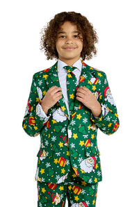 A child with curly hair is dressed in a "Santa Elves Green - Christmas suit" by Suitmeister, featuring decorations of Santa Claus, snowflakes, stars, and gift motifs. They stand smiling against a white background while holding the lapels of the suit's jacket.