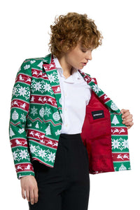 A person sporting the Suitmeister Christmas Green Nordic Jacket, a festive blazer adorned with a red, green, and white Christmas pattern, reveals the jacket's red lining. They have curly hair and are paired with a crisp white shirt and black pants.