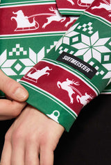 A close-up of a person's hand adjusting a Christmas Green Nordic Jacket - Christmas blazer, featuring festive red and green patterns with reindeer, snowflakes, and sleighs. The label reads Suitmeister.