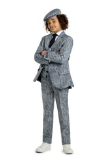 A child with curly hair is wearing the Suitmeister 20's Gangster Grey Halloween suit, complete with a matching flat cap and white sneakers. They are standing confidently with arms crossed against a white background.