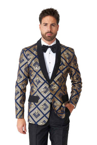 A man wearing the Art Deco Deep Navy prom suit by Suitmeister, featuring a geometric-patterned tuxedo jacket with black lapels and gold and blue designs, complemented by a black bow tie. He has short hair and a trimmed beard, standing against a plain white background.