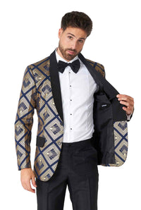 A man with dark hair is wearing the Art Deco Deep Navy Prom suit by Suitmeister. The blazer features a patterned gold and black design, worn over a white shirt with a black bow tie. He is holding one side of the blazer open to showcase its black lining.