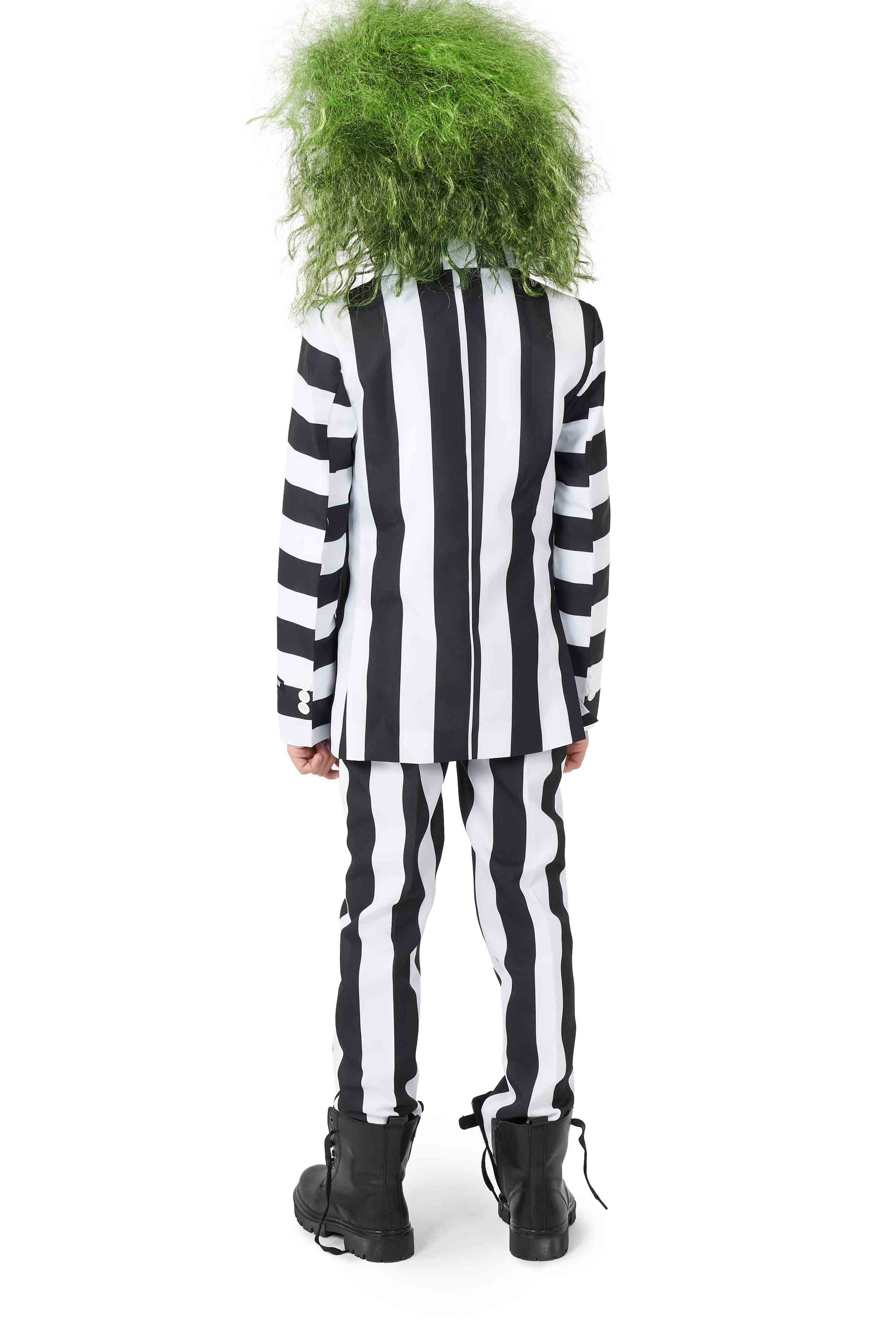 A person in a Beetlejuice suit by Suitmeister, featuring long sleeves and pants with black and white stripes, stands facing away. They have shaggy green hair and are wearing black boots.