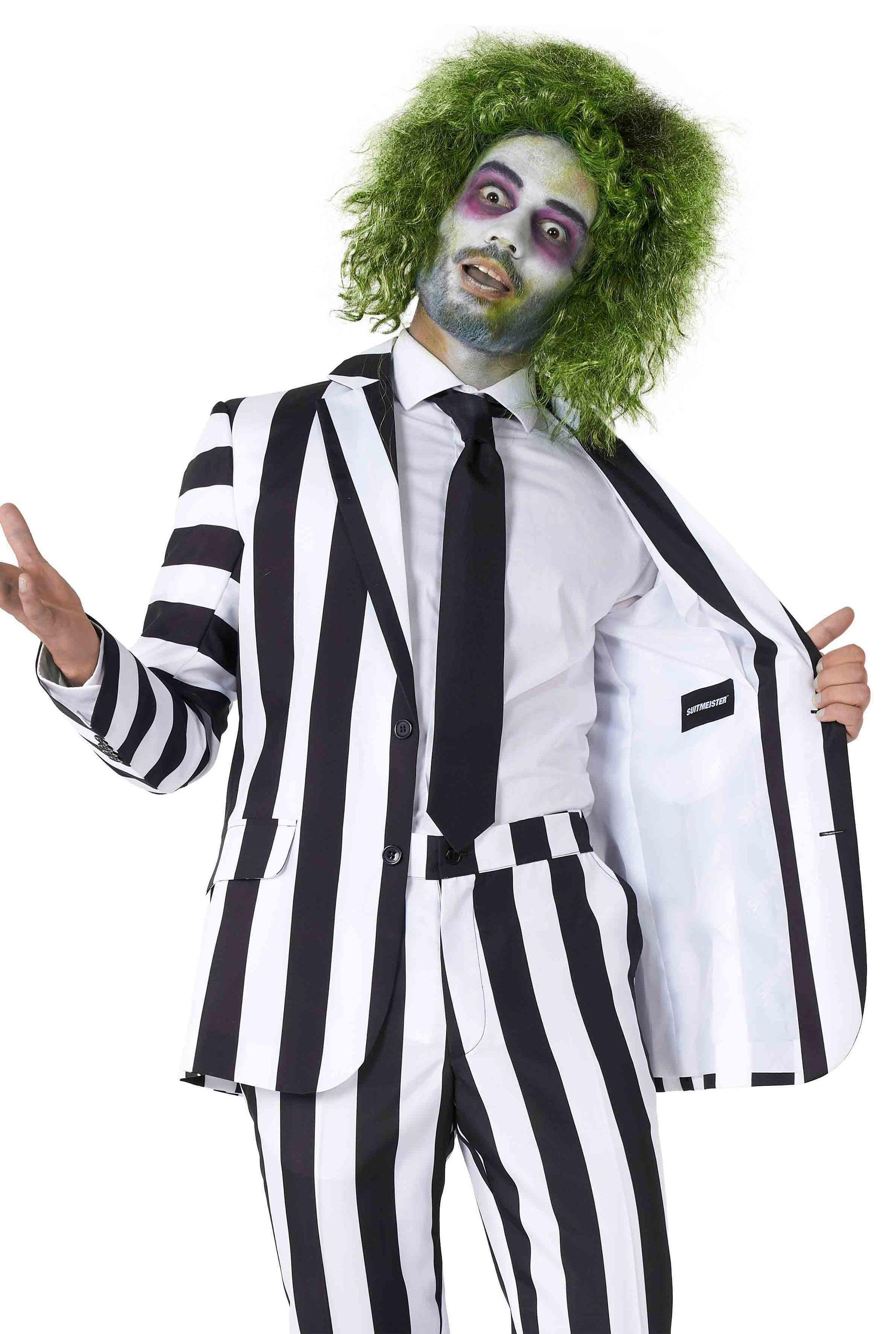 A person dressed in a Beetlejuice costume by Suitmeister is wearing a black and white vertically striped suit paired with a white shirt and black tie. They sport green, frizzy hair and have facial makeup for a ghostly look, while they hold their suit jacket open.