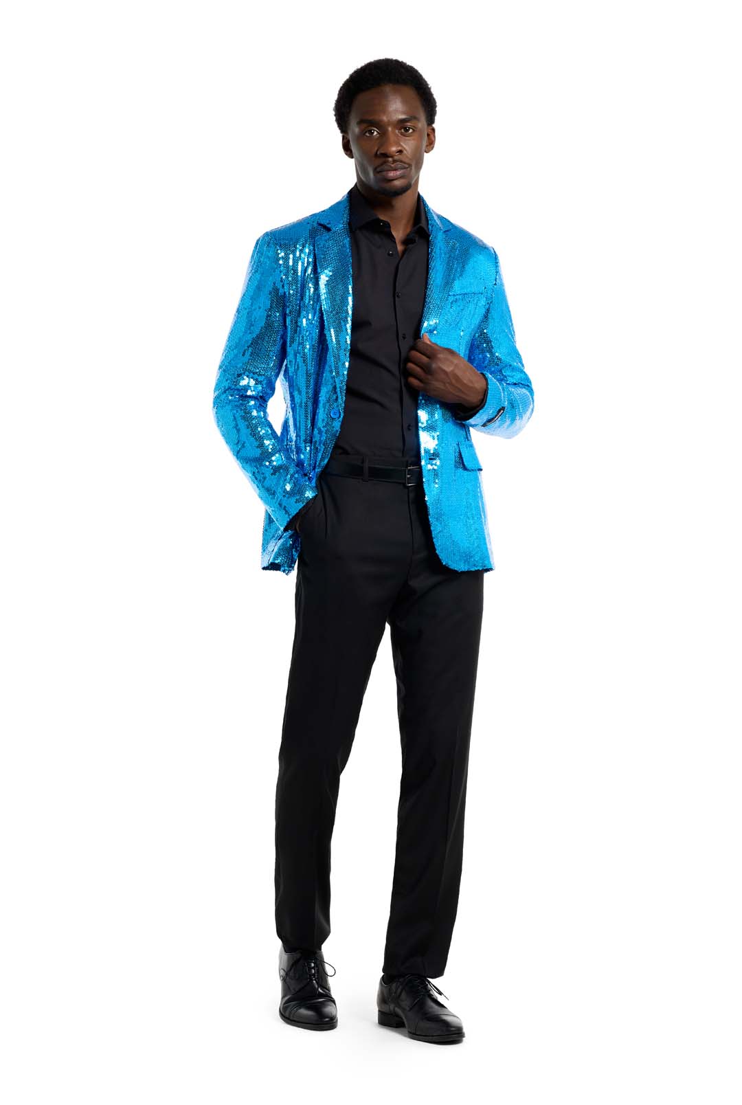 A man stands confidently wearing the Sequins Blue Blazer by Suitmeister, which shimmers brightly over a black shirt and pants. He poses with one hand in his pocket and the other adjusting the blazer against a plain white background.