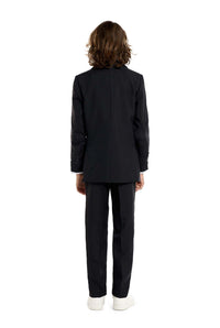 A person with long brown hair, wearing a Suitmeister Solid Black suit and white sneakers, stands facing away from the camera against a plain white backdrop.