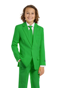 A young person with wavy hair smiles at the camera, wearing a Suitmeister Solid Green suit, white shirt, and green tie. They stand against a white background with one hand in their pocket.