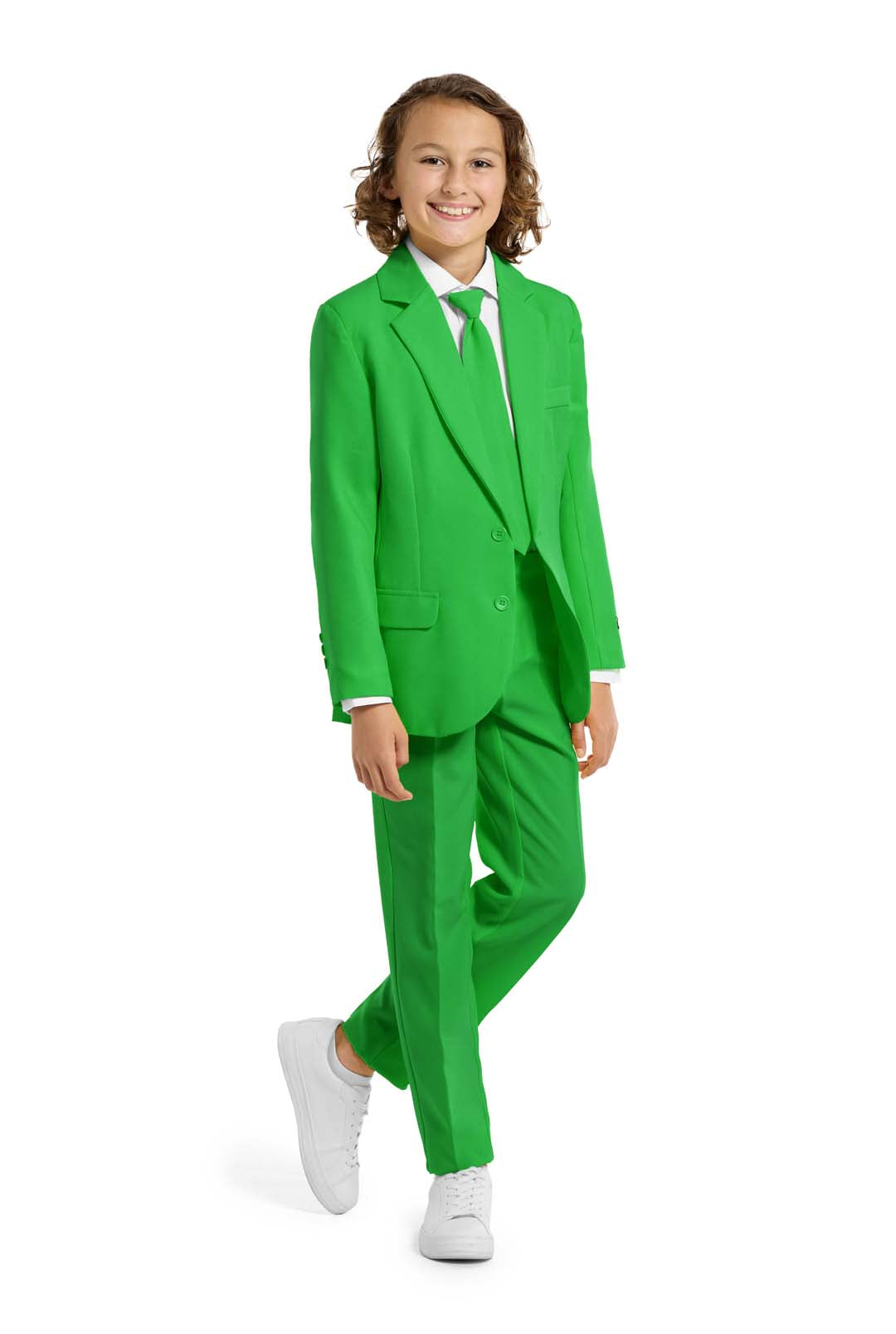 A child with curly hair is joyfully wearing a Suitmeister Solid Green suit, complete with a matching tie and white dress shirt. White sneakers complete the look as they stand against a plain white background.