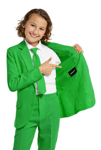 A child in a Suitmeister Solid Green suit and tie points to the inside jacket label against a plain white background, smiling brightly.