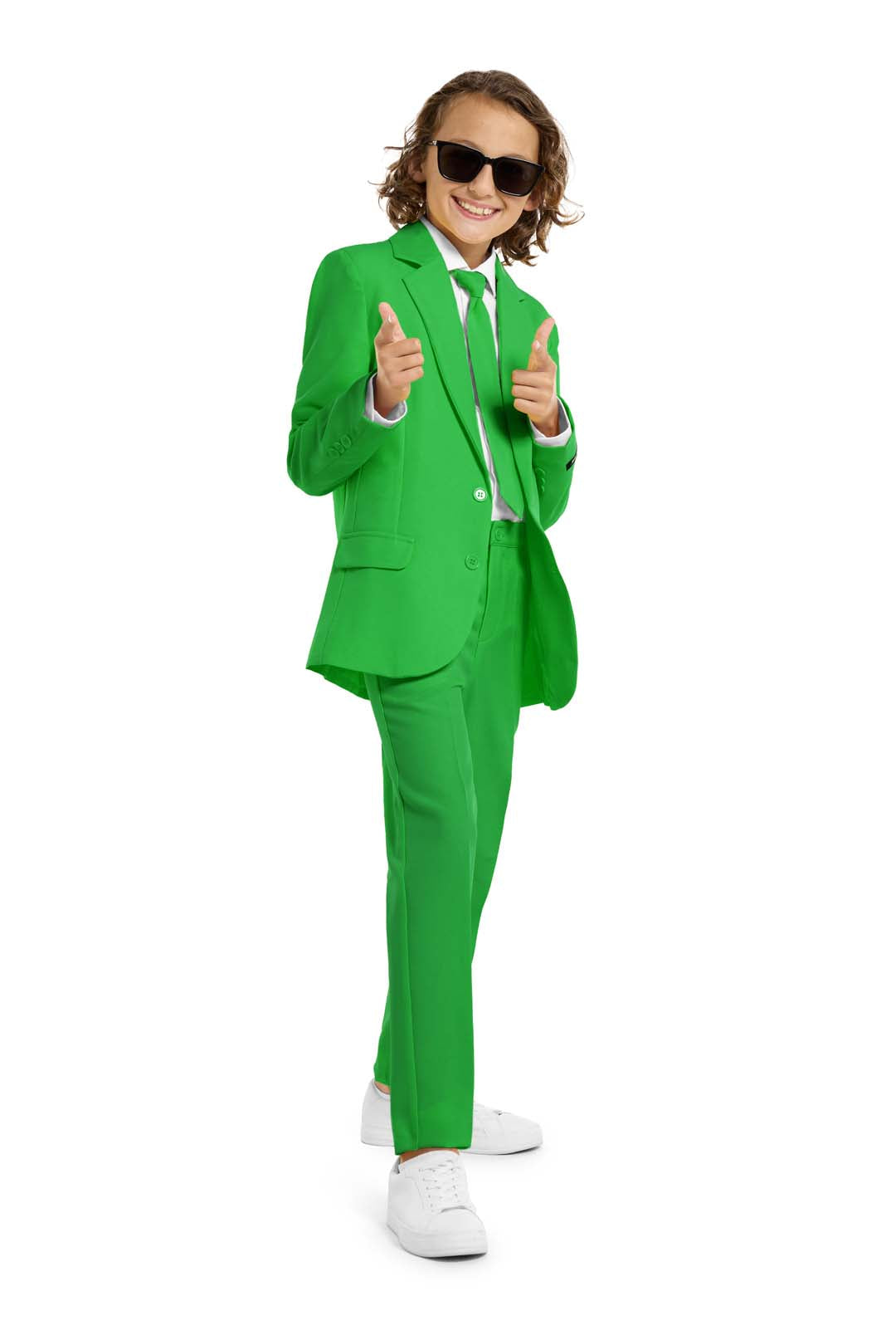 A confident young person showcases the Suitmeister Solid Green green suit, pairing it with white shoes and sunglasses. They pose with a cheerful expression, pointing fingers forward against a plain white background.