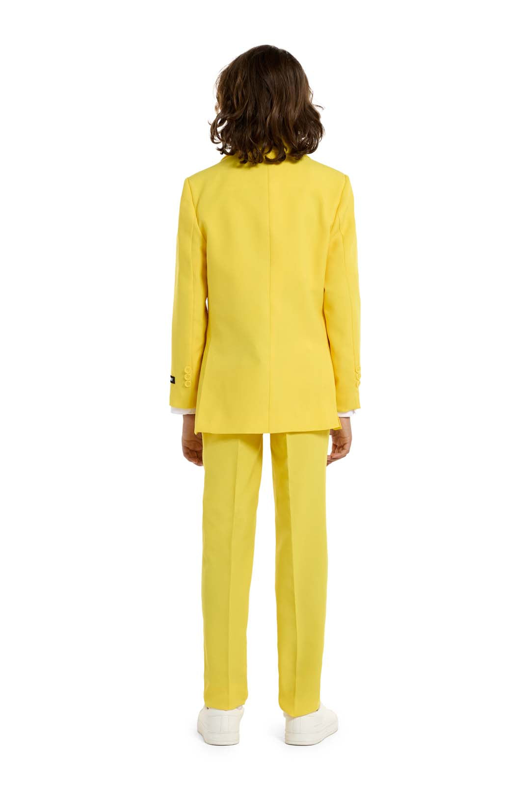 A person with long hair, dressed in the Suitmeisters Solid Yellow suit and white sneakers, stands facing away against a white backdrop.