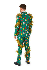 A man is dressed in the Suitmeister Christmas Deco Green - Ugly Christmas suit, showcasing vibrant Christmas-themed patterns such as baubles and snowmen. Gold tinsel adorns the ensemble. He stands with his back to the camera against a simple white background.