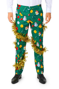 A person dressed in the vibrant Christmas Deco Green suit by Suitmeister, featuring colorful holiday-themed designs like snowmen and ornaments. The outfit is complemented by shiny gold tinsel wrapped around the pants. They are also wearing a white shirt and black shoes.