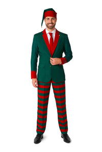 A man dressed in the Suitmeister Santa's Elf Green - Christmas Elf Suit, featuring a green jacket and red tie, complemented by striped red and green pants and a matching hat. He is smiling while adjusting the jacket with one hand, embodying an elf's festive attire.