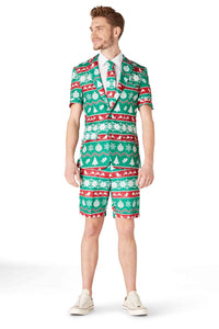 A man is wearing the Suitmeister's "Christmas Green Nordic" suit, a festive ensemble with Christmas-themed patterns of ornaments, snowflakes, and stripes in green, red, and white. He stands against a white background, complemented by a light blue shirt and tie along with white sneakers.