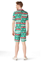 The individual is turned away from the camera, dressed in a vibrant Christmas suit featuring trees, snowflakes, and ornaments. The ensemble consists of a short-sleeved shirt and matching shorts from the Christmas Green Nordic collection by Suitmeister, paired with white shoes.