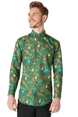 A smiling person wearing the Suitmeister Christmas Green Tree Shirt, which features colorful and playful patterns of birds, leaves, and ornaments, paired with black pants. The background is plain white.