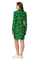 A person with long hair is wearing the Green trees - Christmas outfit from Suitmeister, featuring a vibrant green dress adorned with a colorful fruit pattern of pears, cherries, and apples. They are standing with their back to us and are sporting white sneakers.