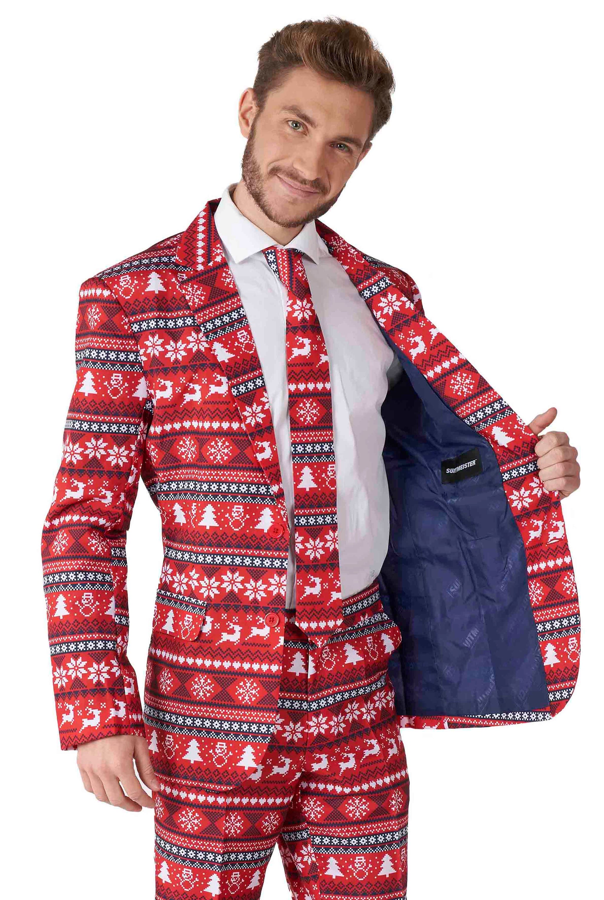 A man beams as he dons the Suitmeister's Nordic Pixel Red - Christmas suit, featuring a festive design with white snowflakes, reindeer, and trees. With one hand, he shows off the suit jacket's blue inner lining.