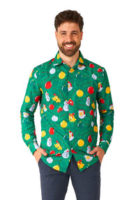 A smiling man with short hair is wearing the Suitmeister Christmas Ornaments Green shirt, featuring colorful holiday-themed designs like snowmen and ornaments. He stands with his hands in his pockets, paired with blue pants.