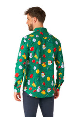 A man is wearing the "Christmas Ornaments Green" shirt by Suitmeister, showcasing festive Christmas-themed designs, including snowmen, ornaments, and reindeer. He stands facing away, displaying the back of the shirt. He's also paired it with dark pants.