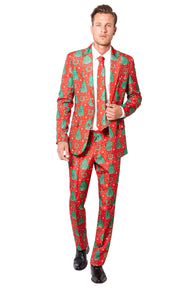 A man wearing the Suitmeister Christmas Trees suit, featuring red and green tree patterns, along with a white shirt and matching tie. He stands adjusting his tie while wearing black shoes.