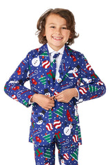 A smiling child wears a Suitmeister Christmas Snowman Blue suit, adorned with festive snowmen, candy canes, Christmas trees, and gift boxes. The child is buttoning the suit jacket over a white shirt and blue tie.