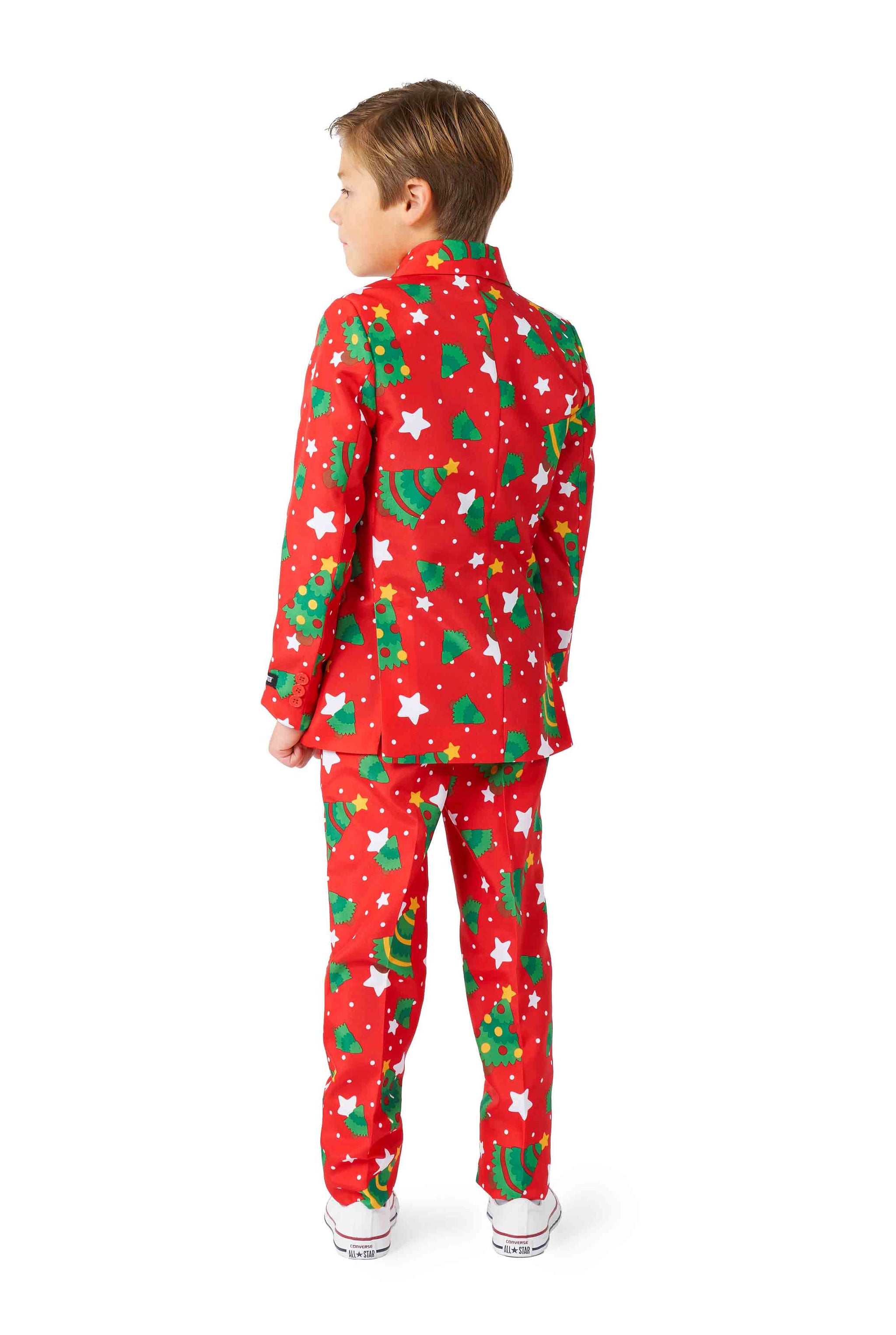 A young child is facing away from the camera, dressed in a Suitmeister Christmas suit called "Christmas Trees Stars Red." The festive outfit features Christmas tree and white star decorations. The child, with short brown hair, stands against a plain white background.