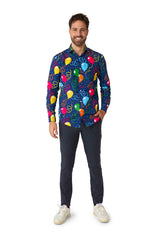 A smiling person stands wearing a vibrant Suitmeister Confetti Balloons shirt, featuring colorful balloons and confetti patterns. With one hand in their pocket, they are dressed in dark pants and white sneakers against a plain white background.