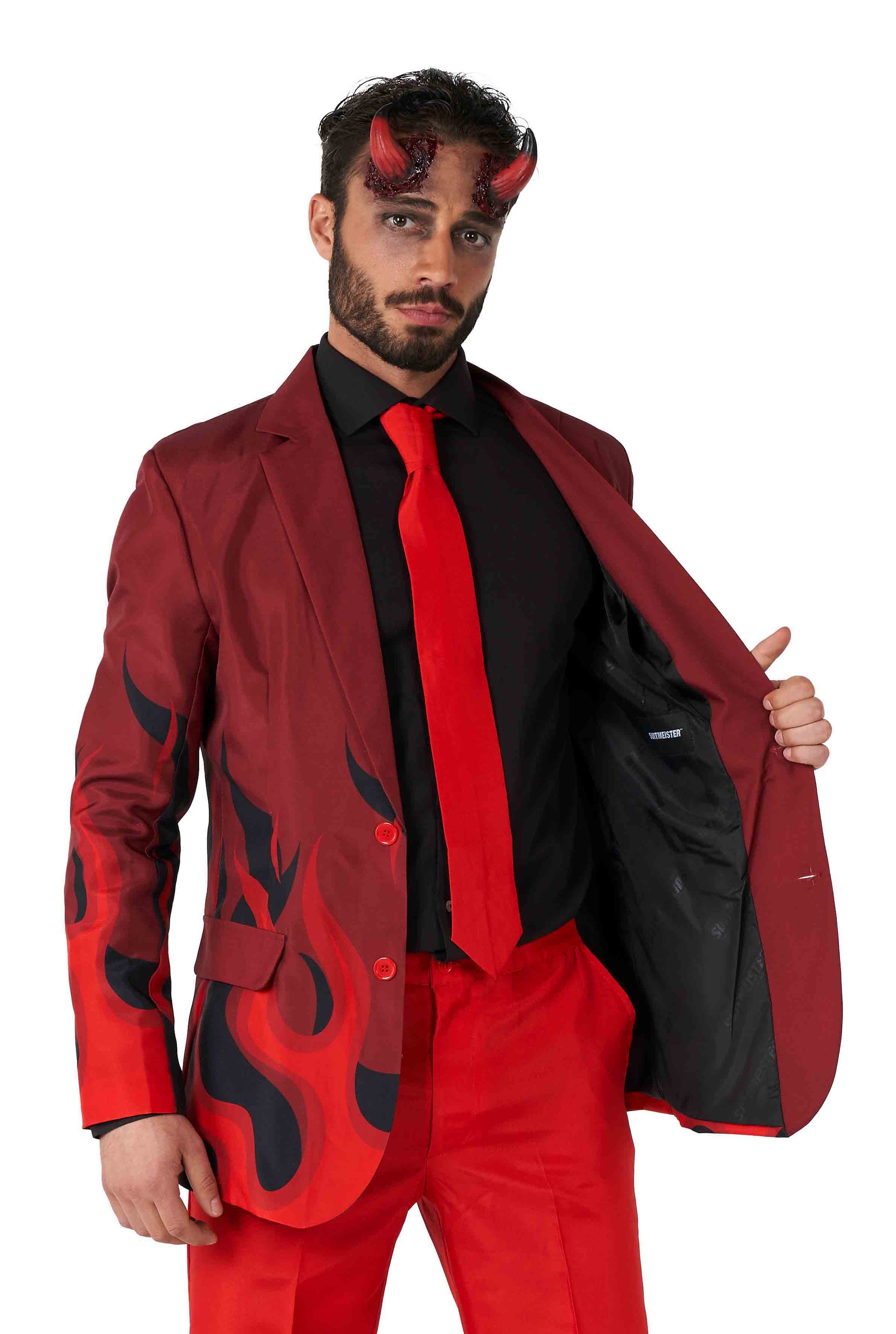 A man with a beard and red devil horns is wearing the Devil Red Halloween suit by Suitmeister, featuring black flame patterns, along with a black shirt and red tie. With a neutral expression, he holds open one side of his jacket.