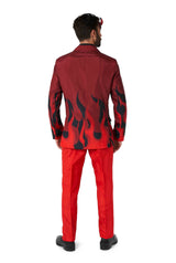 A person stands facing away, dressed in the Devil Red Halloween suit by Suitmeister, featuring black flame designs on the sleeves and lower back. They also have devil horns adorning their head. The suit includes bright red pants, complemented by black shoes.