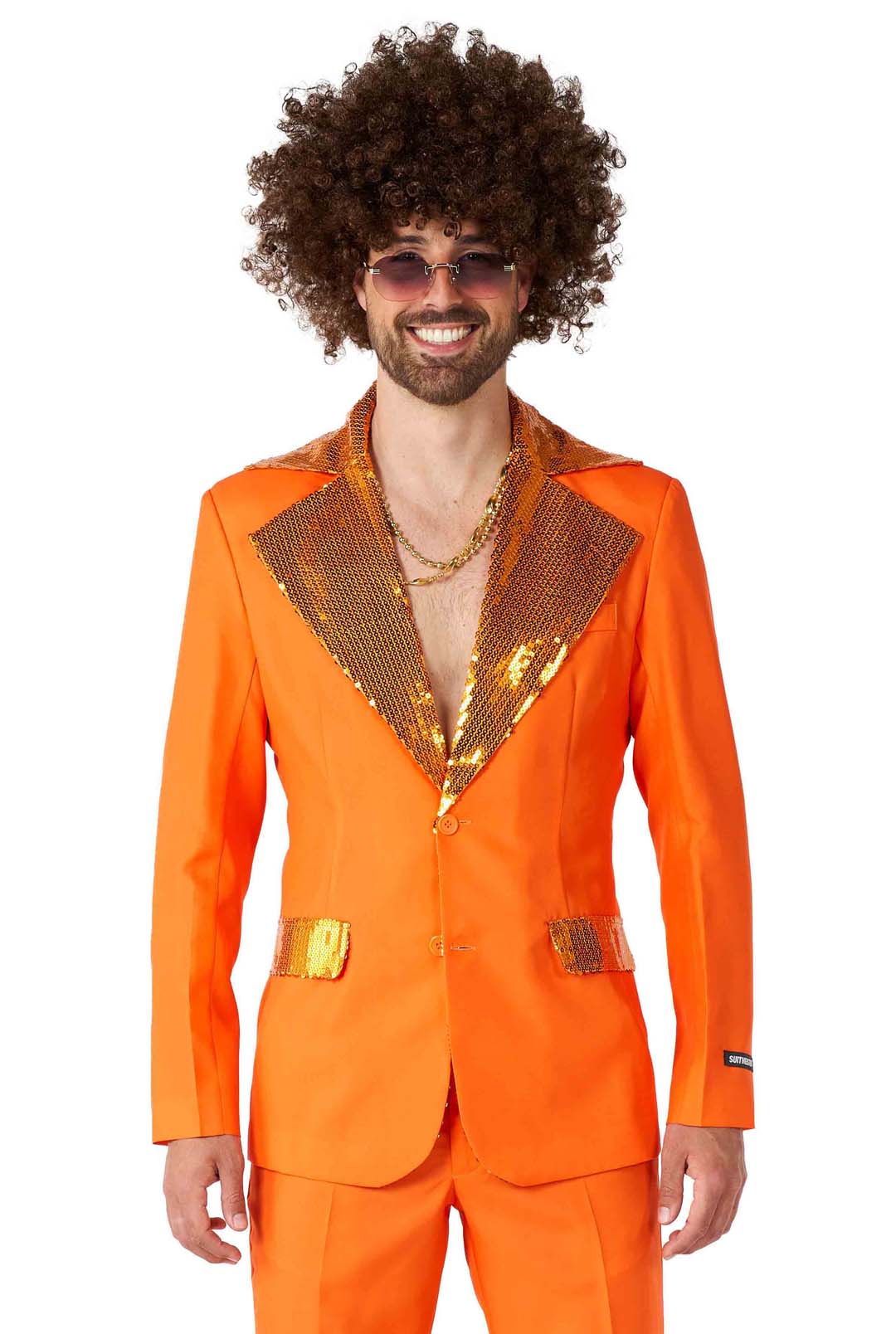 A man dressed in the Disco Suit Orange by Suitmeister, featuring shiny lapels and pockets, smiles at the camera while wearing a curly wig and sunglasses. He completes his retro, disco-inspired look with gold chains.