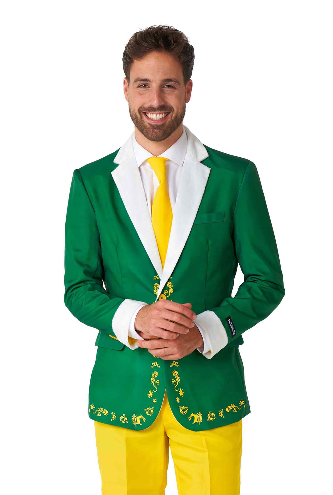 A man smiles, dressed in the Elf™ - Christmas Suit by Suitmeister, featuring a green blazer with ornate gold embroidery, a white shirt, and a bright yellow tie. He pairs it with matching yellow pants, standing with his hands clasped in front of him against a plain white background.