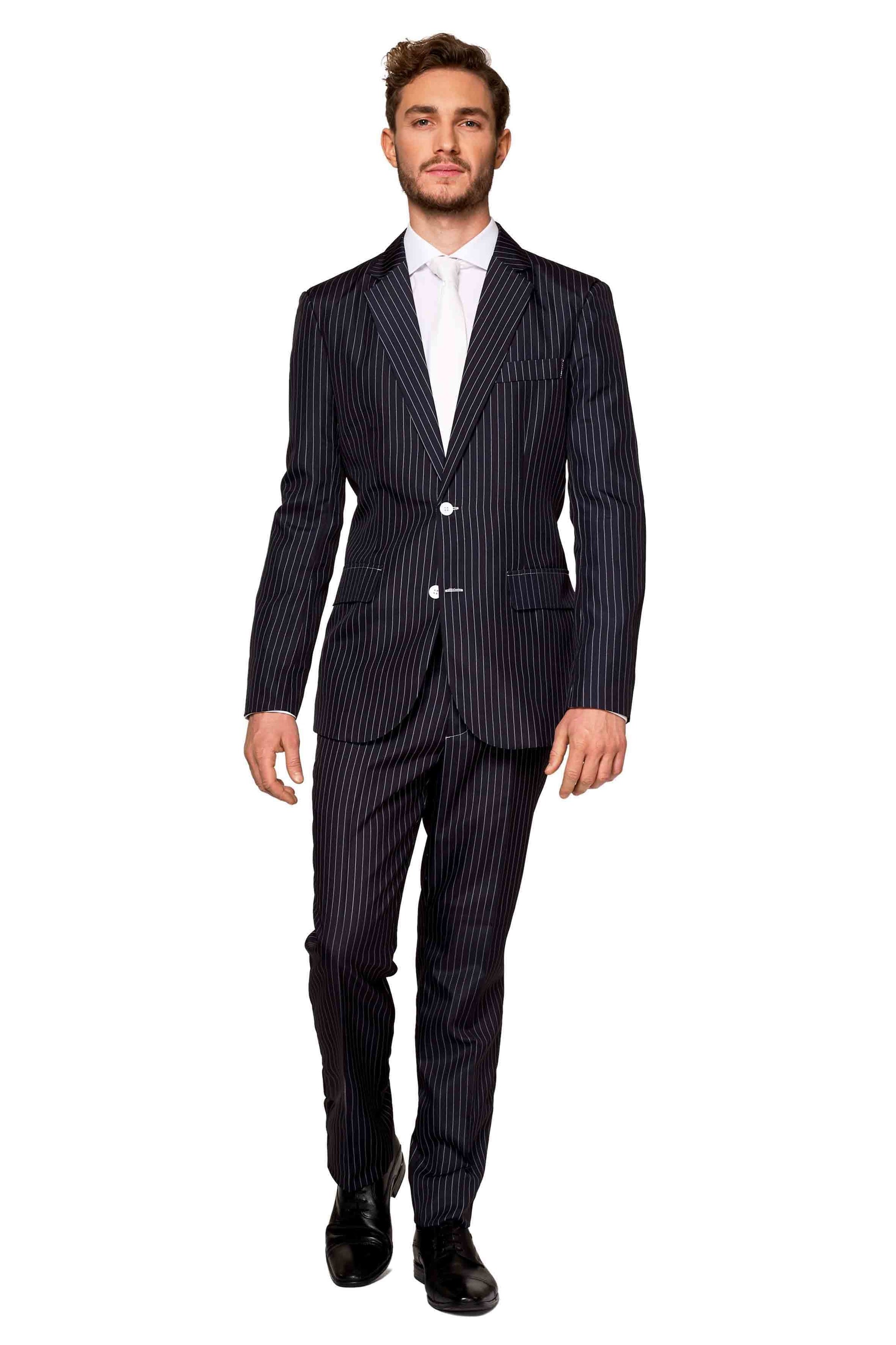 A person dressed in the Gangster Pinstripe Black suit by Suitmeister, complemented by a white shirt and tie, strides confidently against a white background. This attire boasts a tailored fit with a single-breasted design, paired with black shoes.