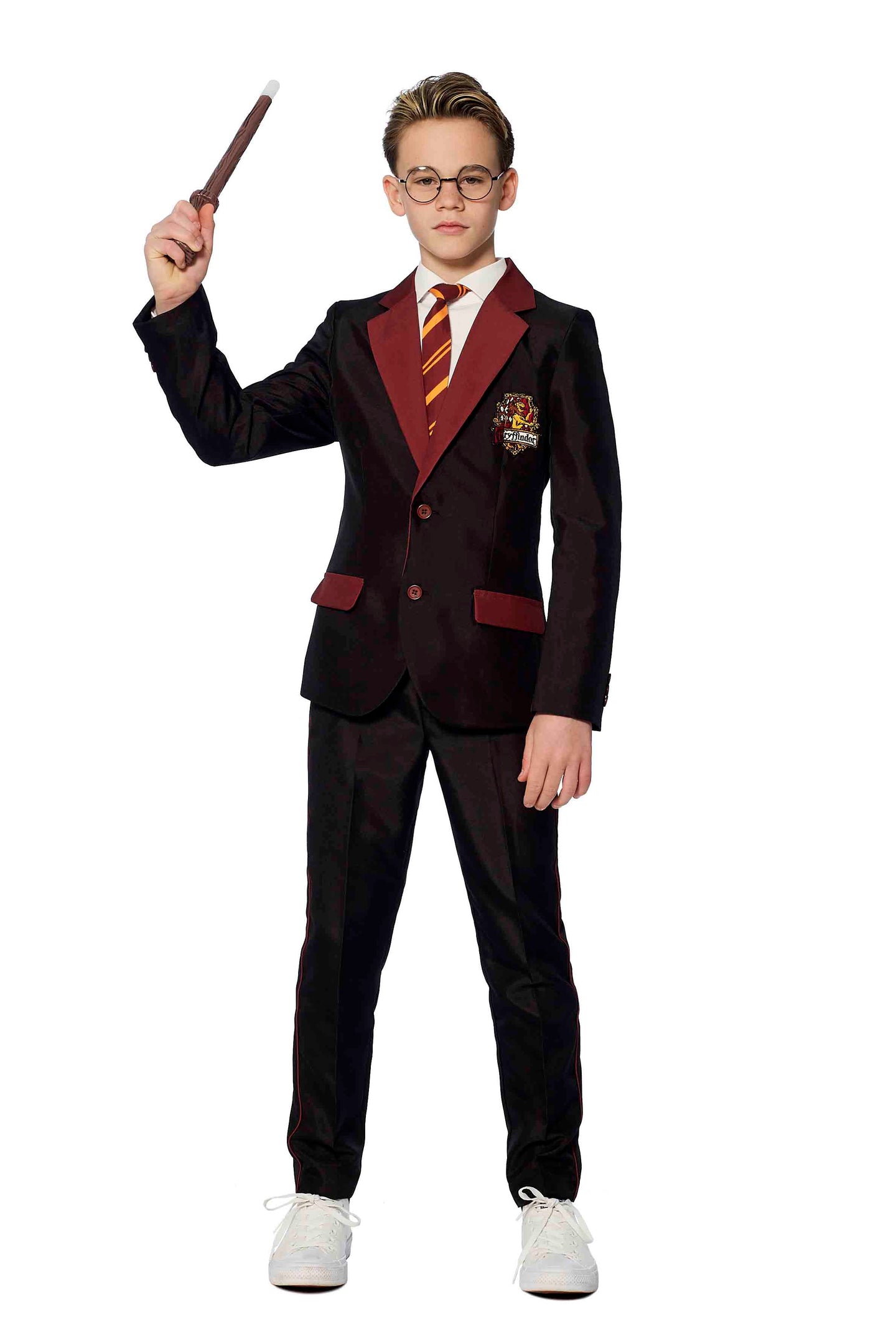 A young person is donning a Suitmeister Harry Potter Gryffindor™ suit, complete with maroon accents and a striped tie. They are wearing glasses and holding a wand in their right hand, standing confidently with their gaze forward.