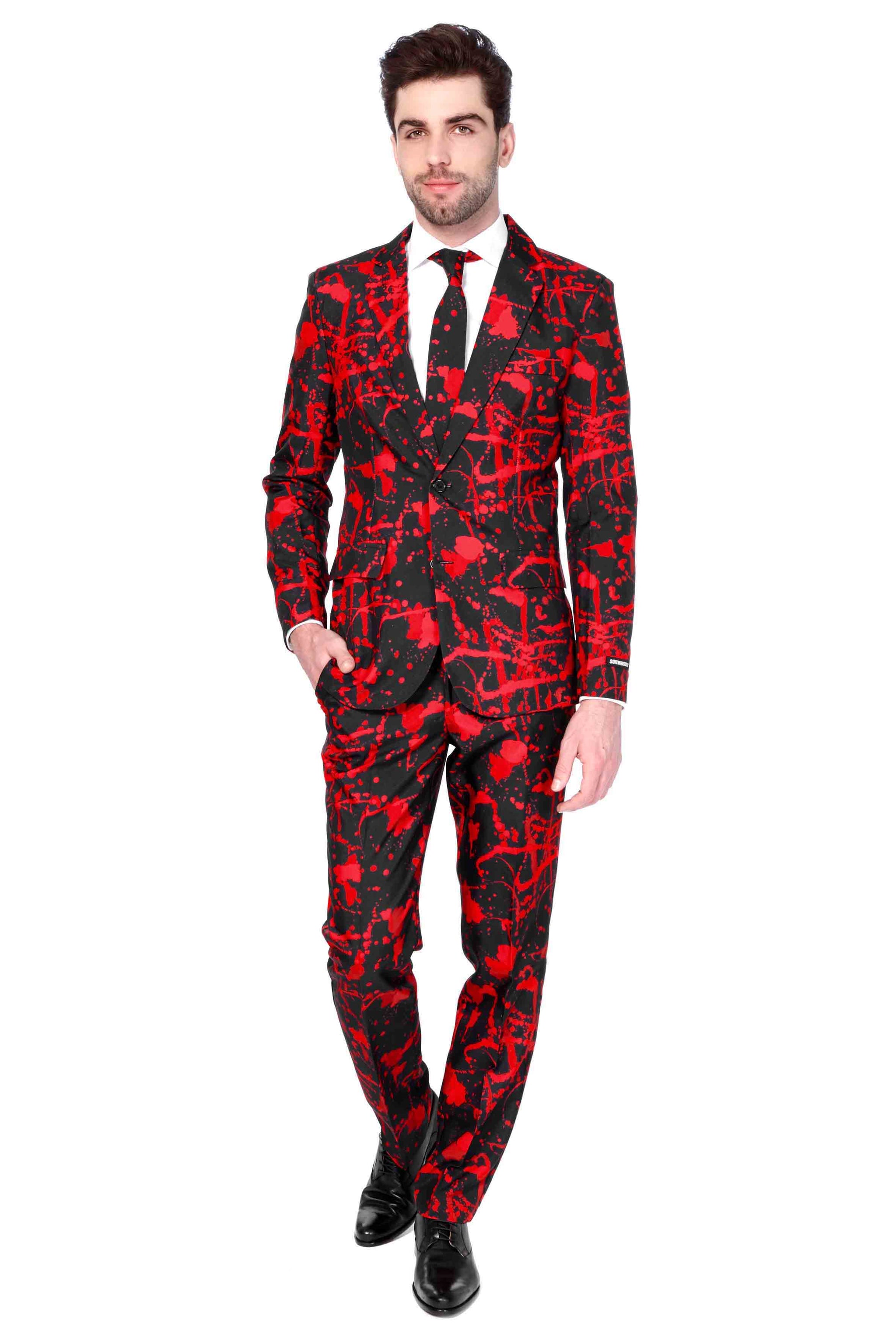 A man is confidently standing with one hand in his pocket, wearing the Halloween Black Blood suit from Suitmeister. The black suit features a bold red abstract pattern, paired with a white shirt and a black tie. He completes the look with black shoes against a plain white background.