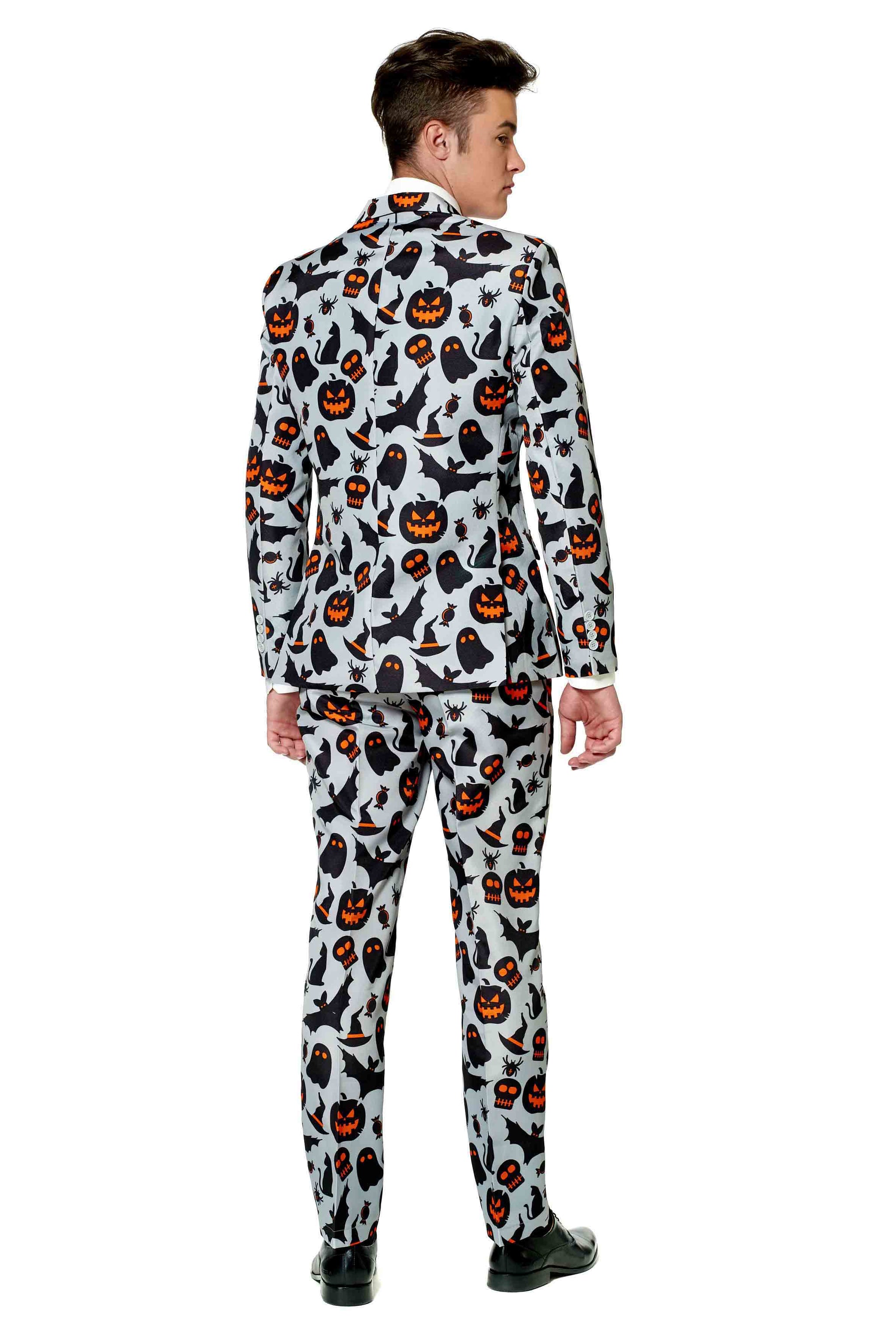 The man stands with his back turned, dressed in the Suitmeister "Halloween Grey Icons" suit, adorned with a Halloween print showcasing black cats, pumpkins, ghosts, and bats. The ensemble is completed by black shoes.