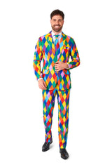 A man smiles while wearing the Harleclown - Mardi Gras suit, a vibrant, multicolored, diamond-patterned ensemble by Suitmeister. He stands against a plain white background.