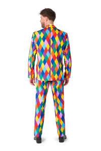 Dressed in a Harleclown - Mardi Gras suit by Suitmeister, a person stands with their back to the camera. This vibrant outfit showcases a multicolored harlequin pattern with diamonds in red, blue, yellow, green, and orange. They pair the ensemble with black shoes and have short hair.