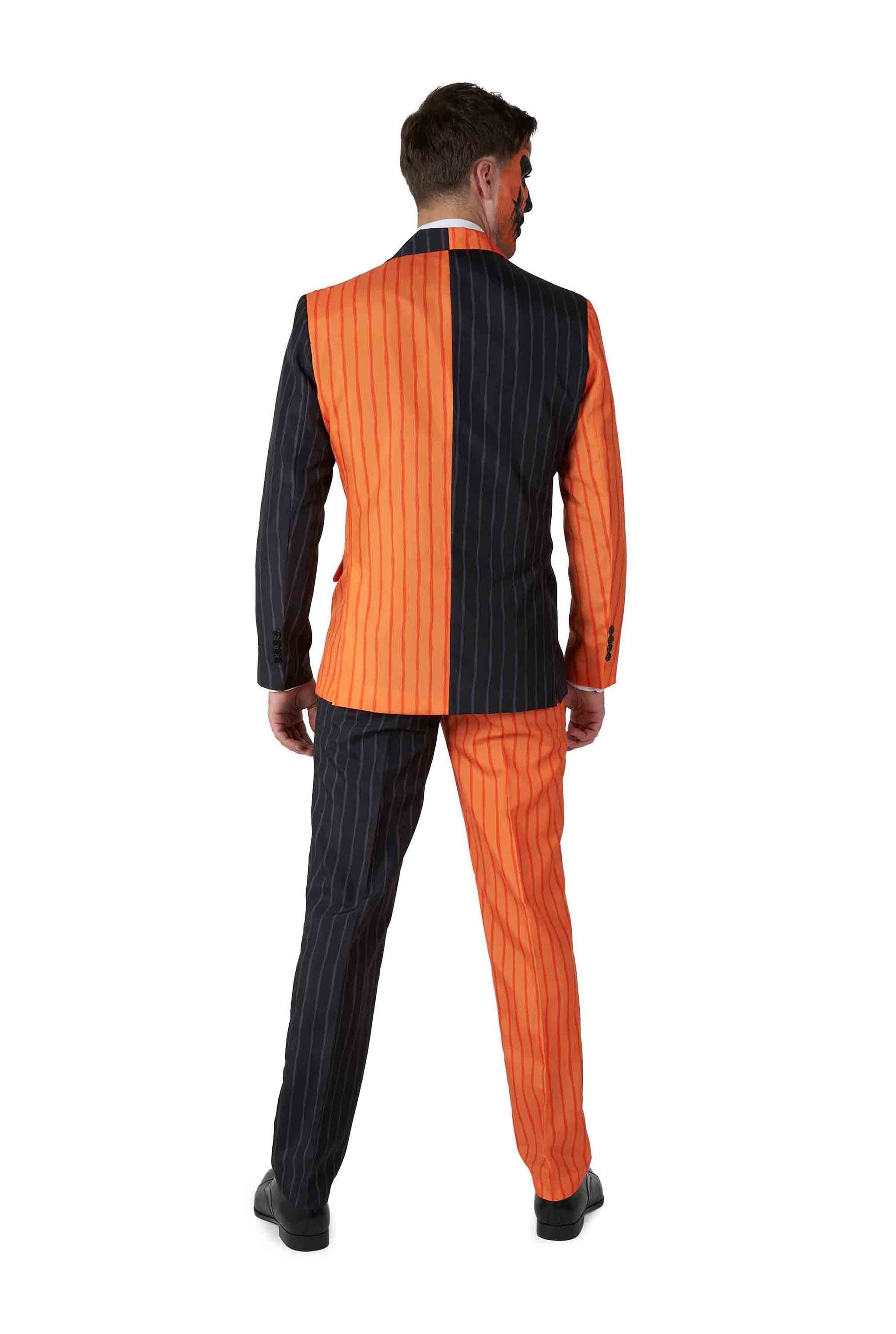 An individual models the Jack-O Pinstripe Black Halloween suit from Suitmeister, featuring a split design with one side in orange with black stripes and the other in black with orange stripes. They pair the look with black shoes and have short, dark hair.