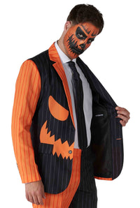 A man dressed in the Jack-O Pinstripe Black Halloween suit by Suitmeister, featuring an orange and black striped pattern with a pumpkin face design. His face is adorned with a matching orange and black jack-o-lantern paint. He is holding open his suit jacket to reveal a name tag inside.