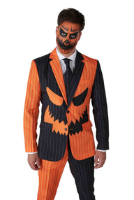 A man is dressed in the Jack-O Pinstripe Black Halloween suit from Suitmeister, featuring orange and black vertical stripes and a stylized pumpkin face design. His face is painted with orange and black makeup to resemble a jack-o-lantern.