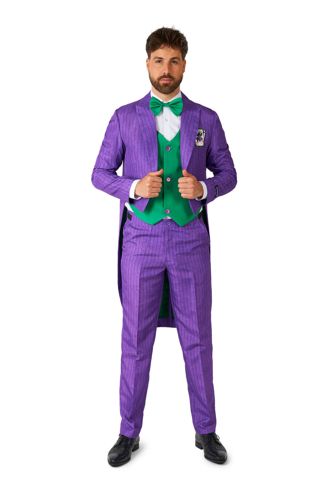 A man stands confidently in a vibrant Joker™ Tailcoat Suit Purple from Suitmeister, featuring eye-catching stripes and matching tails. He pairs it with a green waistcoat and bow tie, gripping the front edges of his jacket with a serious expression. His outfit is completed with black shoes, and he has neatly styled hair.