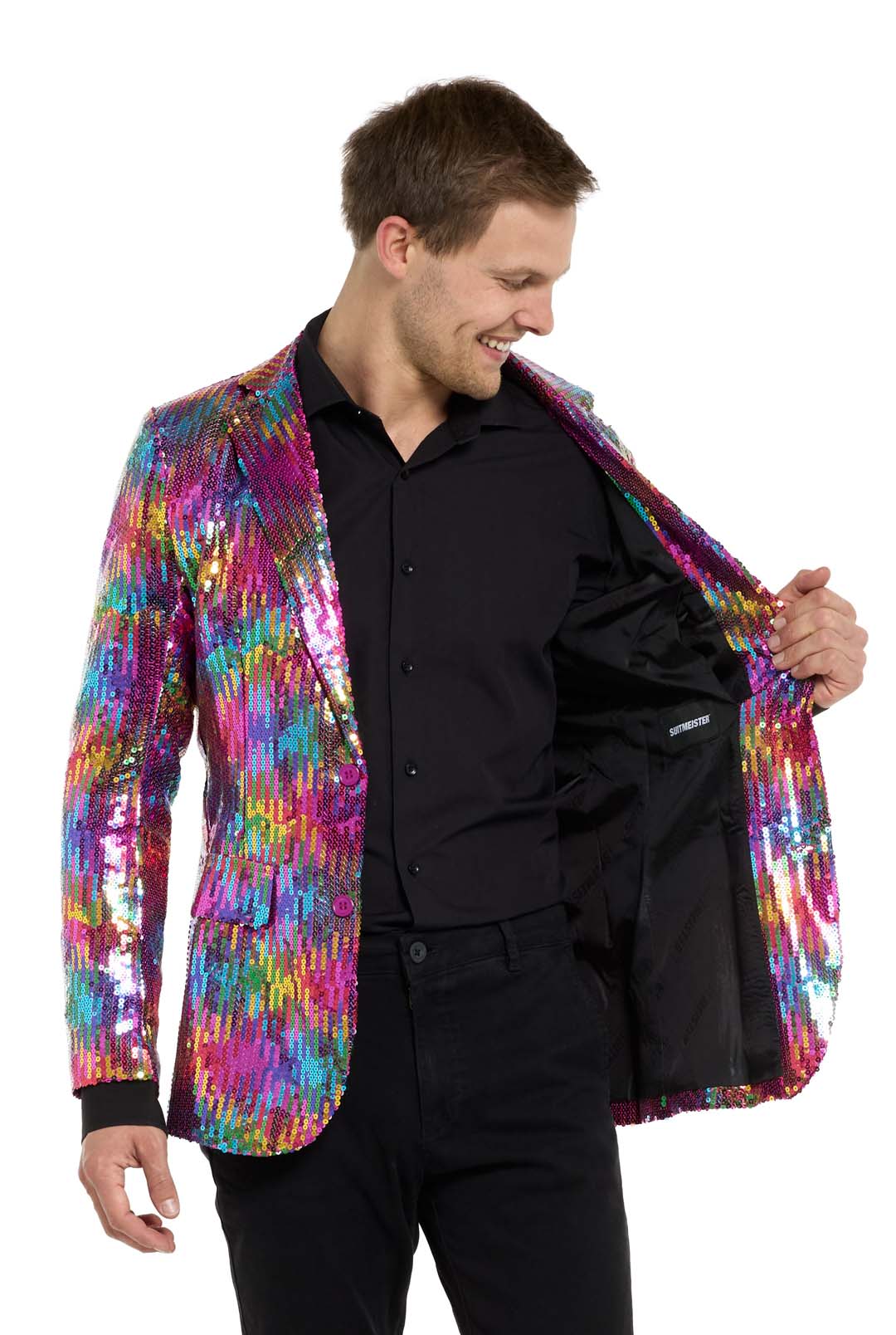 A man grins as he opens his Suitmeister Rainbow Sequin Blazer, revealing its black interior. The blazer, with pink, blue, and gold hues in a vivid pattern, complements his black shirt and pants.