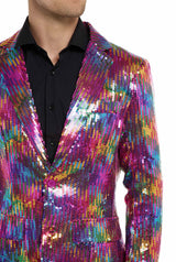 A person in Suitmeisters Rainbow Sequin Blazer sparkles with shades of pink, blue, gold, and green over a black shirt. The focus is on their upper body and clothing, with the face partially visible.